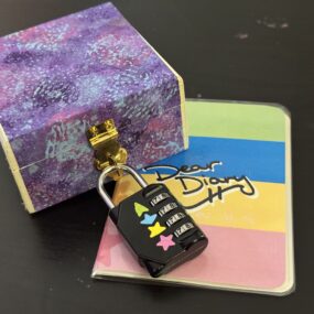 A locked box sits atop a colorful journal that says "Dear Diary"